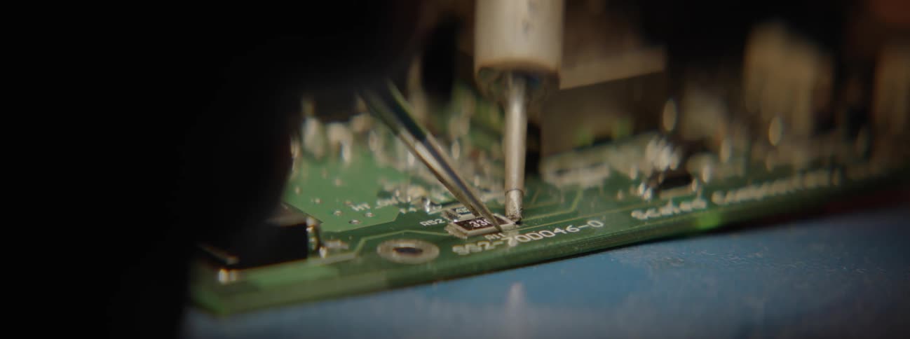 A person soldering an electrical component while holding a tweezer