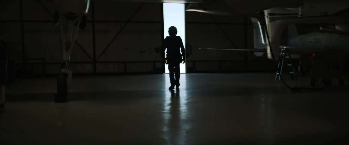 The silhouette of a male pilot is seen as he walks through the doors of an aircraft hangar