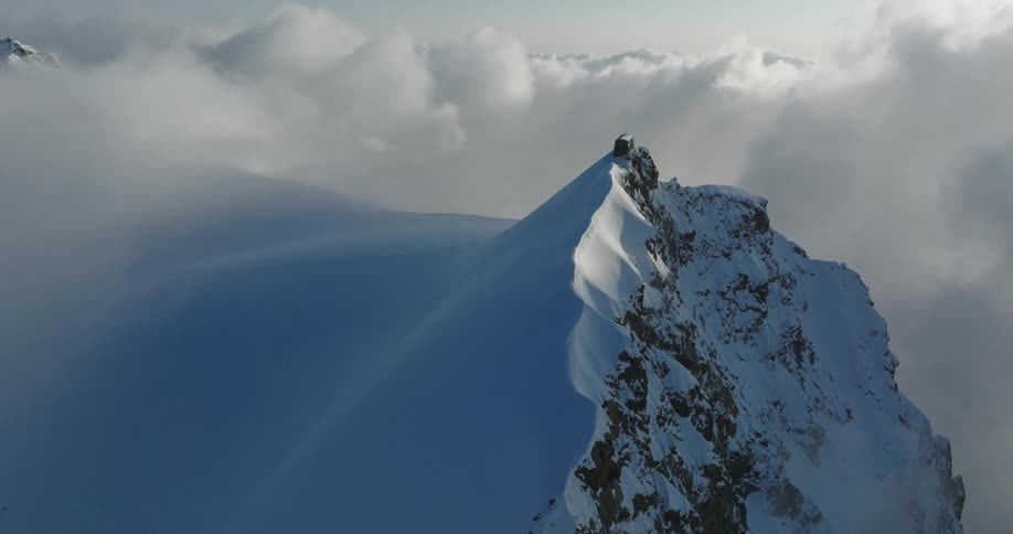 Aerial view of mountains at cloud level covered in snow on a sunny day