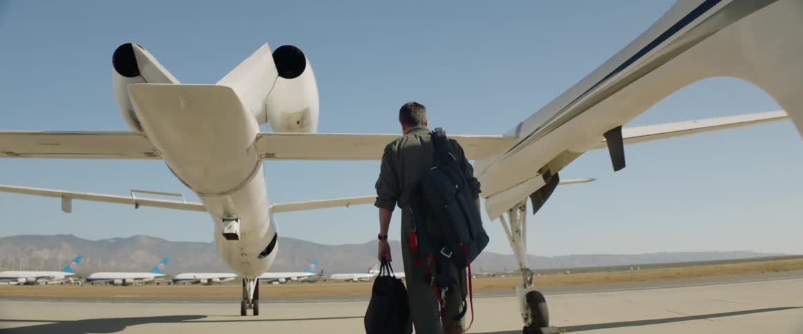 A male pilot walks along the tarmac leading towards the cockpit of a uniquely designed airplane