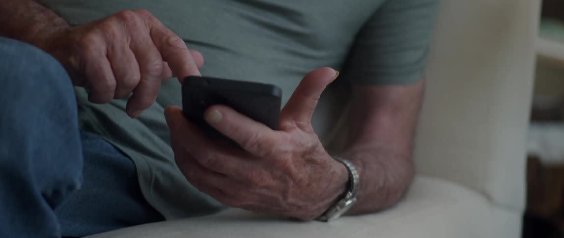 An old man sitting down fiddling with a cell phone with his fingers