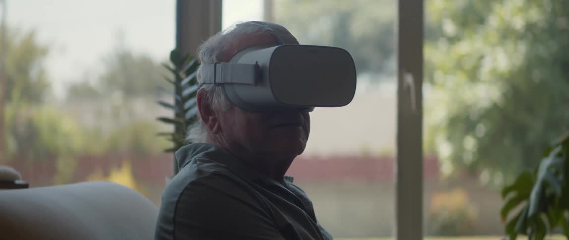 Old man with a virtual reality headset sitting on a couch indoor