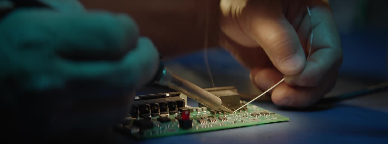 Man using soldering iron on a circuit board at night