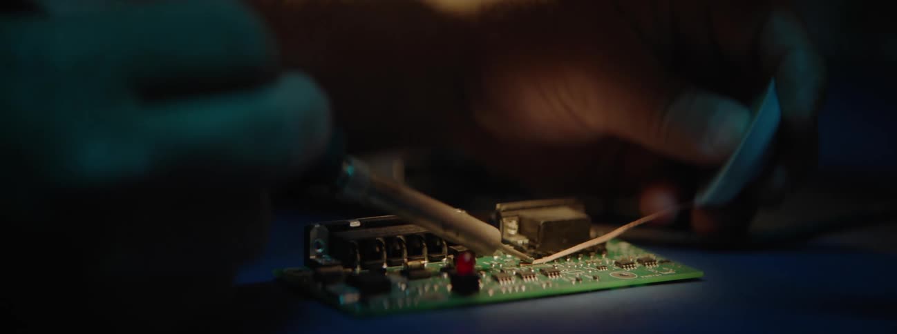 Man using soldering iron on a circuit board in the dark