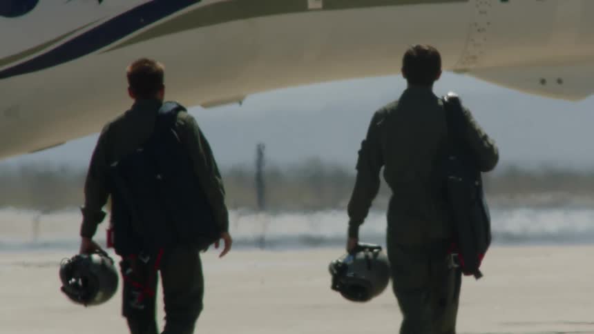 Two pilots walking towards the aircraft with backpacks on their backs and holding their safety helmets