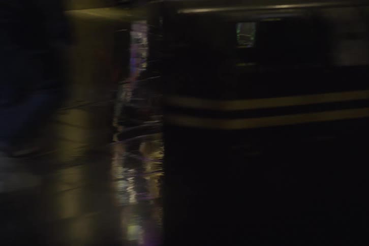 Numerous people walk alongwet city sidewalk at nighttime