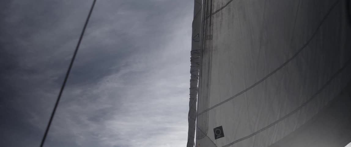 The sail of a boat is blowing in the wind on a cloudy day