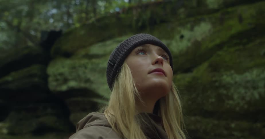 A young blonde woman in the middle of a forest looking upwards