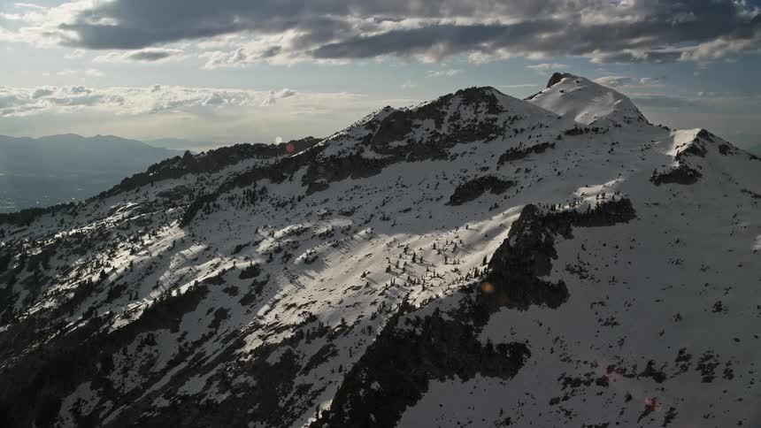 Aerial footage of Lone Peak in snowy Wasatch Range Utah showcasing a winter landscape with snow-covered mountain peaks and partly cloudy skies