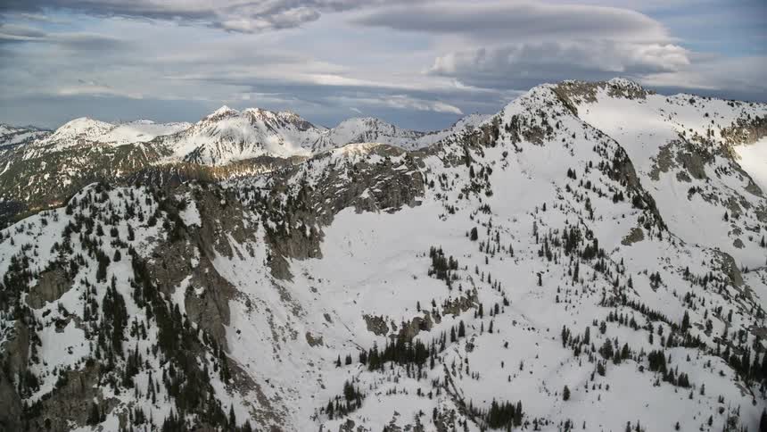  aerial footage showcases snow-covered mountain ridges in the Wasatch Range Utah during wintertime with partly cloudy skies
