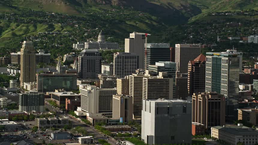 A stunning aerial view of downtown Salt Lake City Utah as the camera flies by towering city buildings revealing the majestic Utah State Capitol in the background on a sunny day