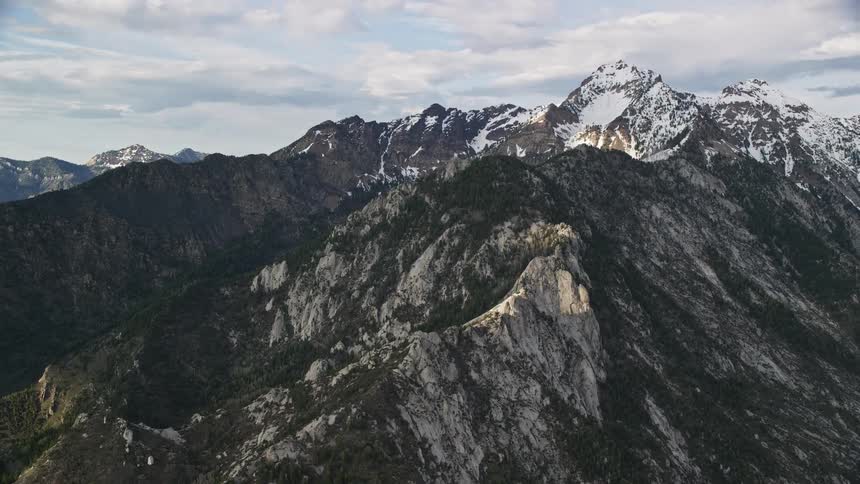 Aerial footage of a snow-covered mountain peak with partly cloudy skies in the Wasatch Range Utah during summertime