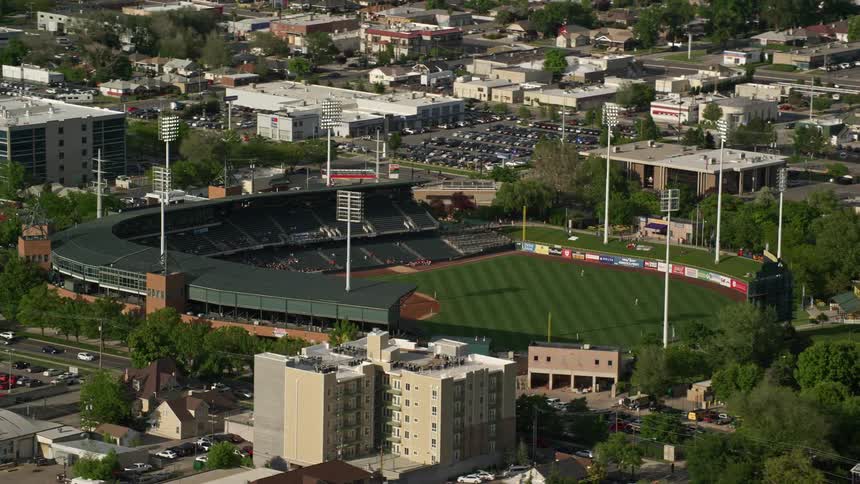 Aerial footage of Spring Mobile Ballpark during a baseball game in Salt Lake City Utah with people in the stands cars driving on the streets and a sunny summer day