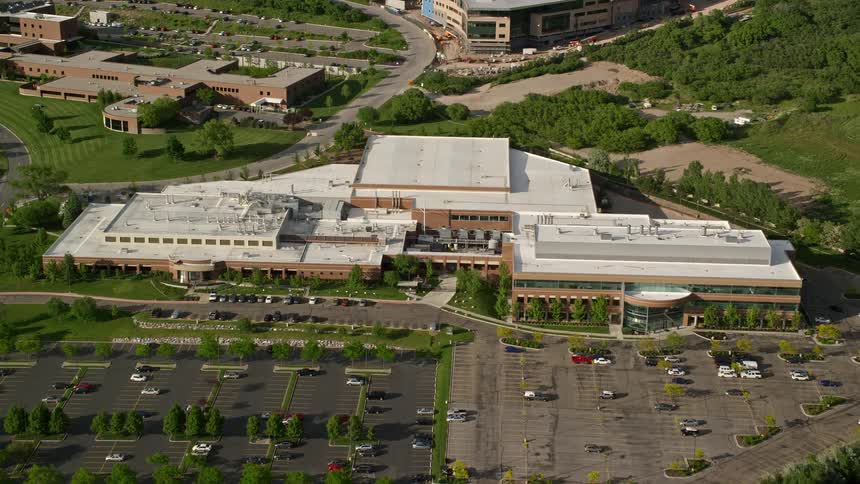 Approaching University of Utah office building from a bird's eye view with a tilt showcasing the sunny Salt Lake City surroundings and bustling parking lots at nearby businesses during summer