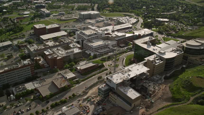 Aerial footage of University of Utah Hospital buildings in Salt Lake City Utah showcasing the surrounding urban neighborhood and fields of grass during summer