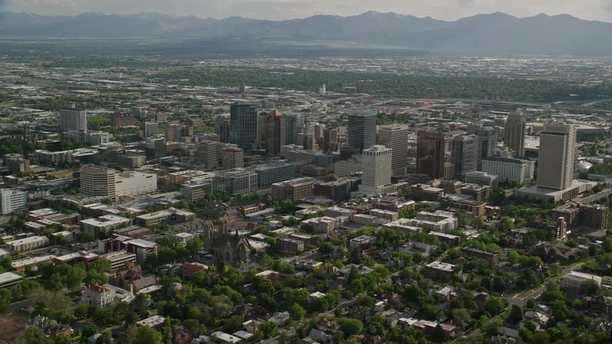 Aerial footage of Downtown Salt Lake City Utah capturing the city streets and buildings against a backdrop of foggy mountains with a partly cloudy sky in the background