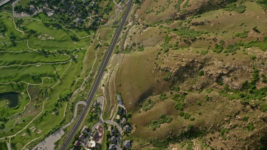 Aerial footage showcasing suburban neighborhoods and houses surrounded by natural vegetation and mountains in Salt Lake City Utah with clear skies and light traffic on I-215