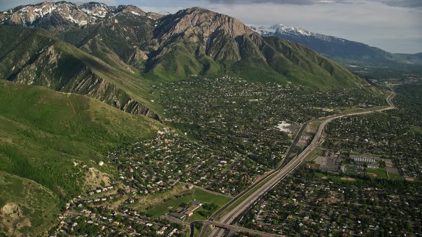 A stunning aerial fly over suburban neighborhoods with a view of the Wasatch Range approaching Salt Lake City Utah under clear skies during summer