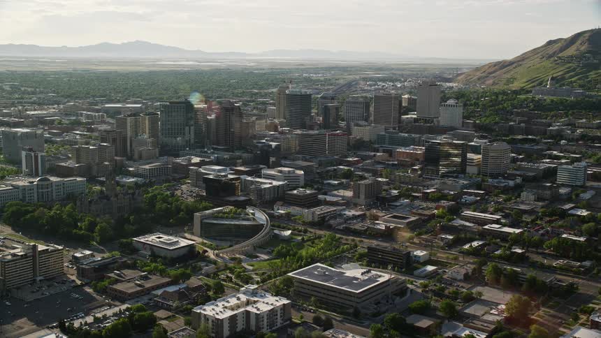 A sunny aerial view of Downtown Salt Lake City Utah as the camera approaches buildings and neighborhoods while flying over the metropolis during a clear day in summer