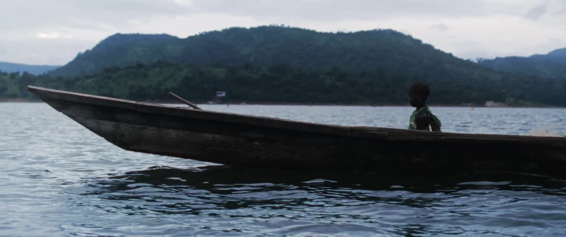 A young child sits alone in a boat in the water