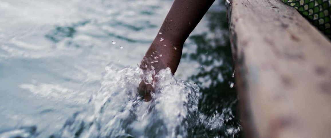 Close up of a persons hand trailing along in the water as they sit in a wooden boat