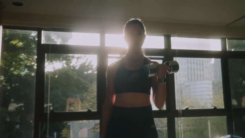 A young woman does bicep curls as she lifts weights