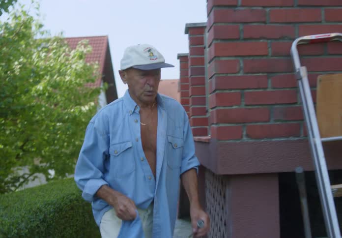 An old man walking into his backyard holding the edge of his shirt