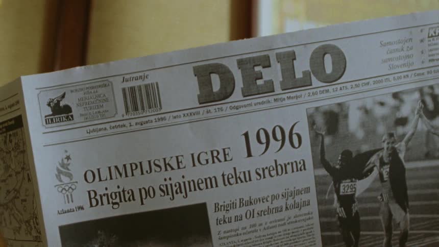 An unseen individual is depicted holding a delo newspaper from 1996 featuring news about the olympic games
