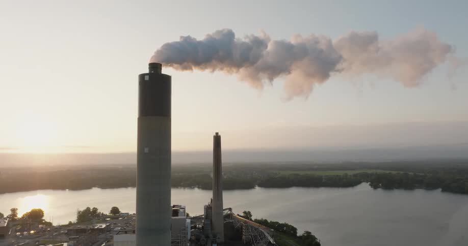 Smoke billows from a tall stack as the sun crests above the horizon