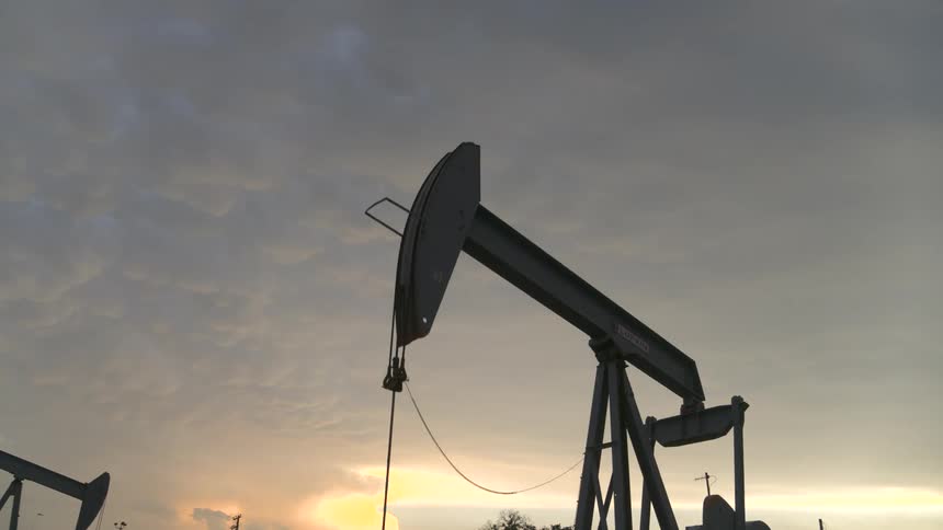 Low angle pullback from the silhouette of a working oil pump at sunrise
