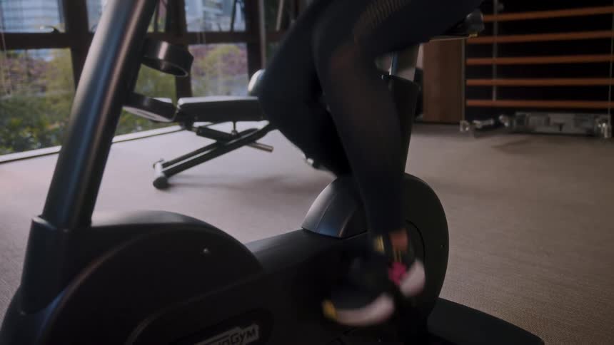 Woman exercises on stationary bike in home gym with window showing city