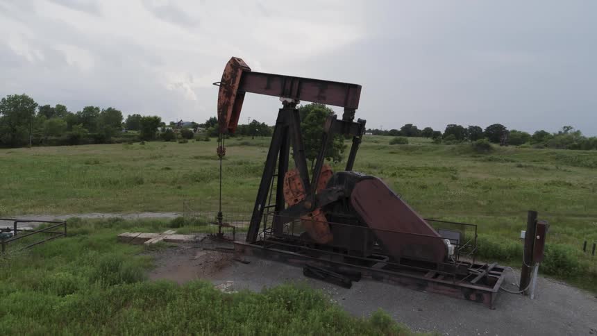 An oil pump operates with a rhythmic motion in the middle of a green field