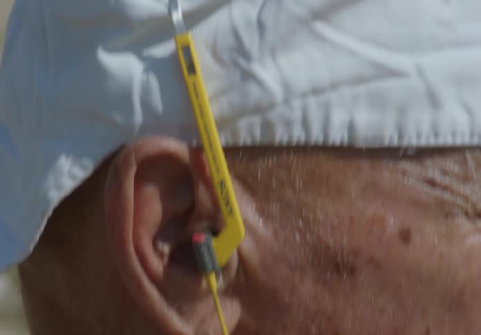 Close up of the side of an older mans face headphones in his ear and a white cap backward