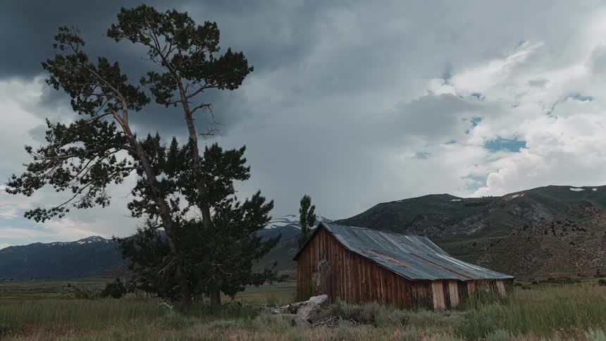 Timelapse of a wooden cabin in a pasture with a mountain range on the horizon