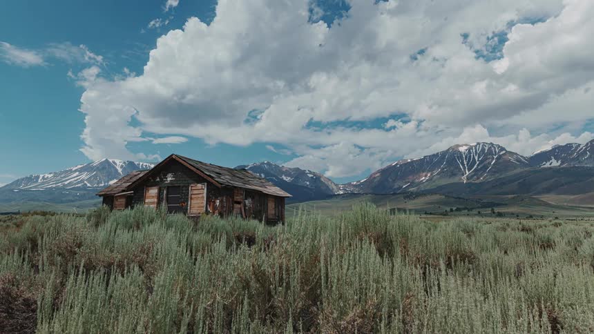 Clouds flow over rural house and nearby mountains and cast shadows