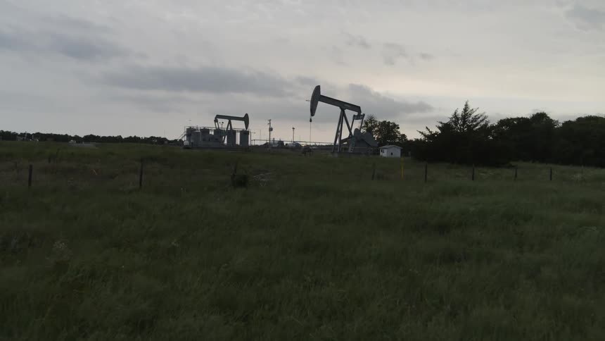 Low approach toward two pumpjacks steadily working along an oil field