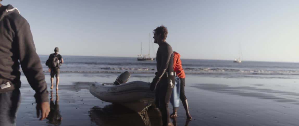 People in wet suits walk around a raft on the beach