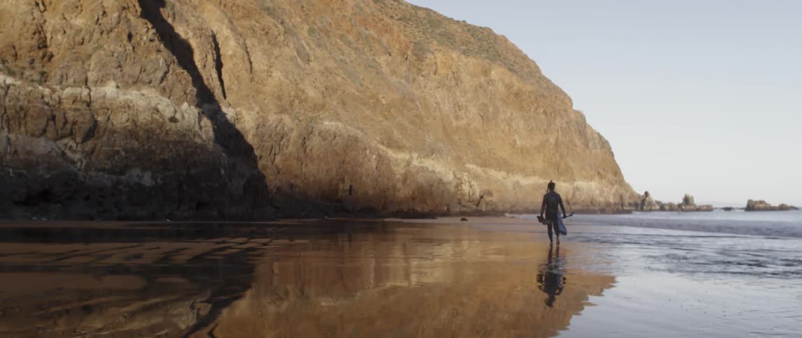 A man is walking by the water on a beach