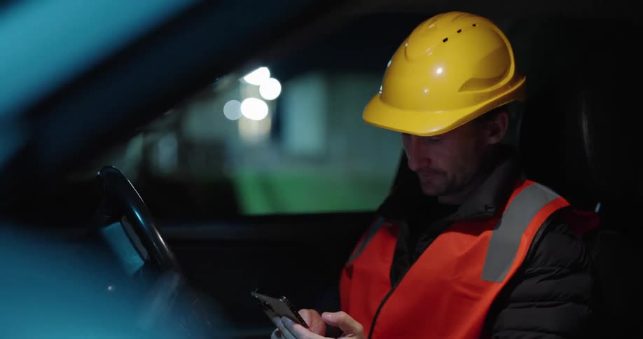 Man in protective clothing and helmet sitting in the car typing on a cellphone