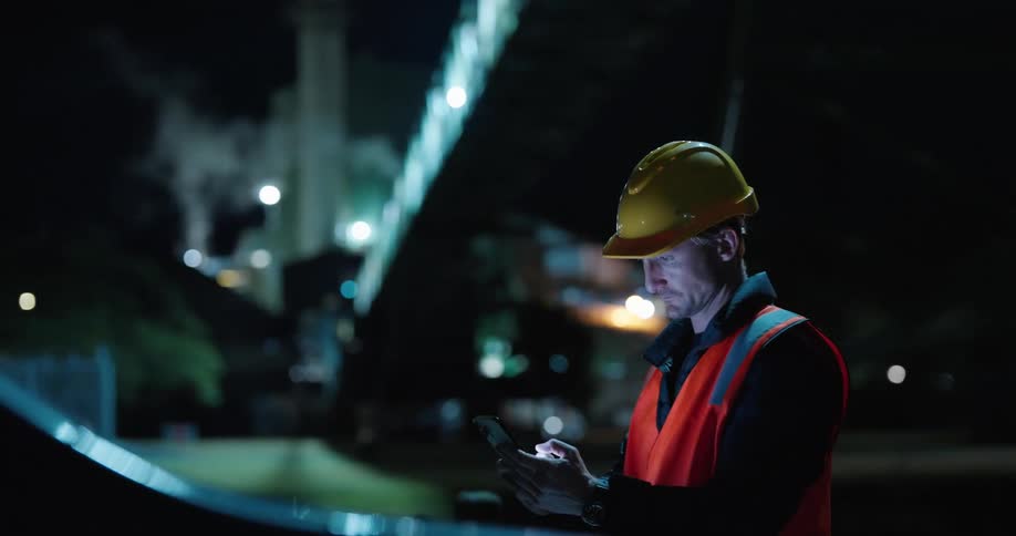 Man wearing a safety helmet and reflective clothing using a cellphone in an outdoor setting at night