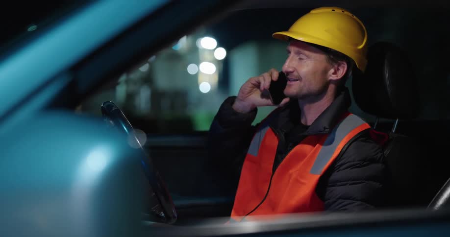 Construction worker speaks on the phone inside a car at night