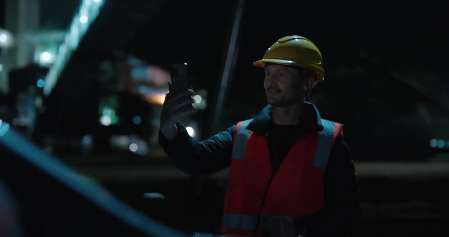 A construction worker is doing a video call at night on his cell phone