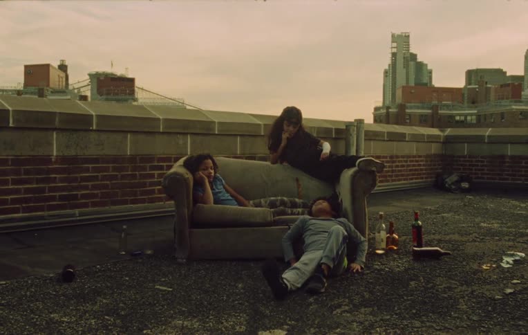 Siblings sit on and near loveseat on building roof near scattered liquor bottles