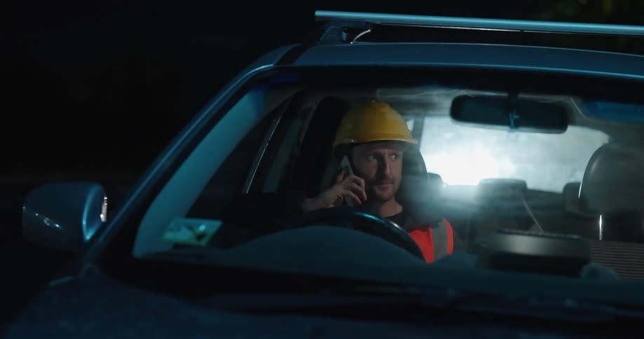 Man wearing a protective helmet sitting in the car and answering the phone during the night
