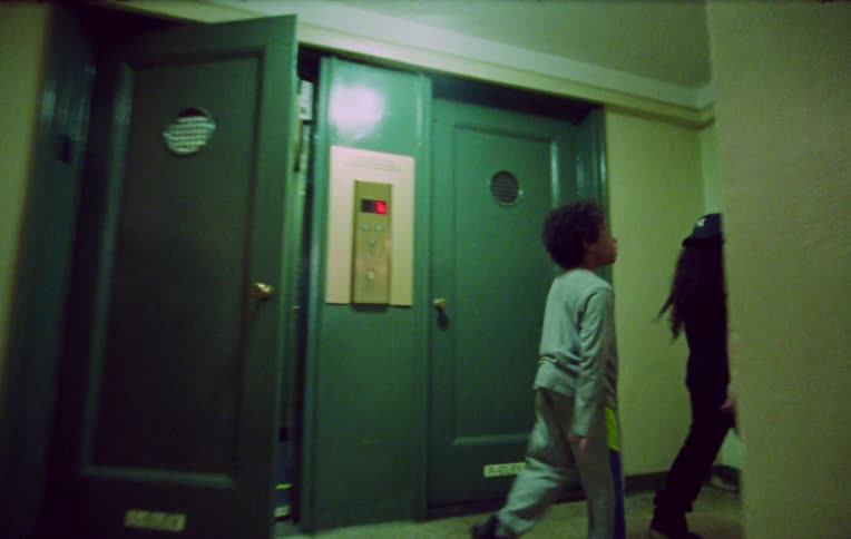 Siblings exit apartment and walk down corridor together
