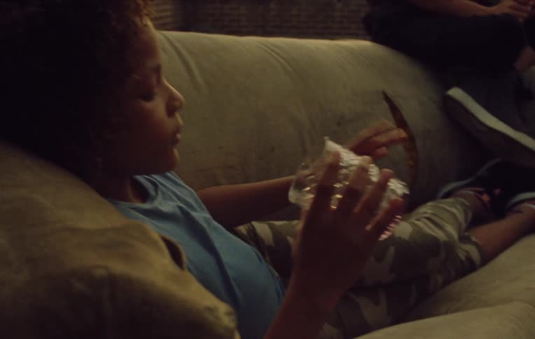 Close up of a girl child laying on a couch then grabbing a glass and looking into it