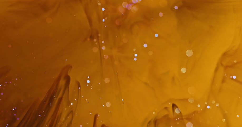 Drop of water falls on dark yellow liquid ink creating ripples
