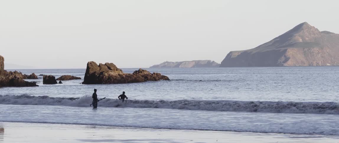 Two people are standing in the surf on a cloudy day