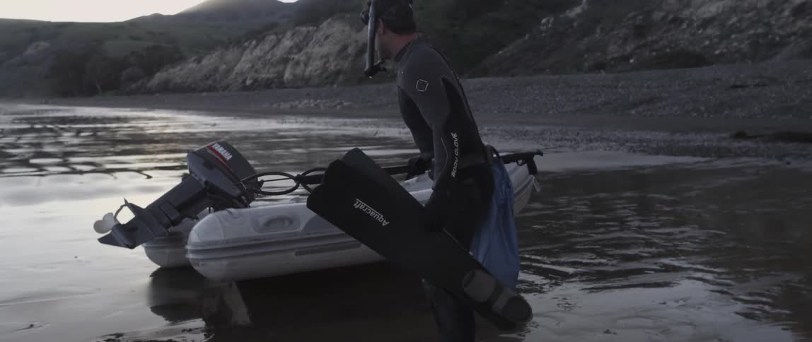 A man in a wet suit puts things into a raft
