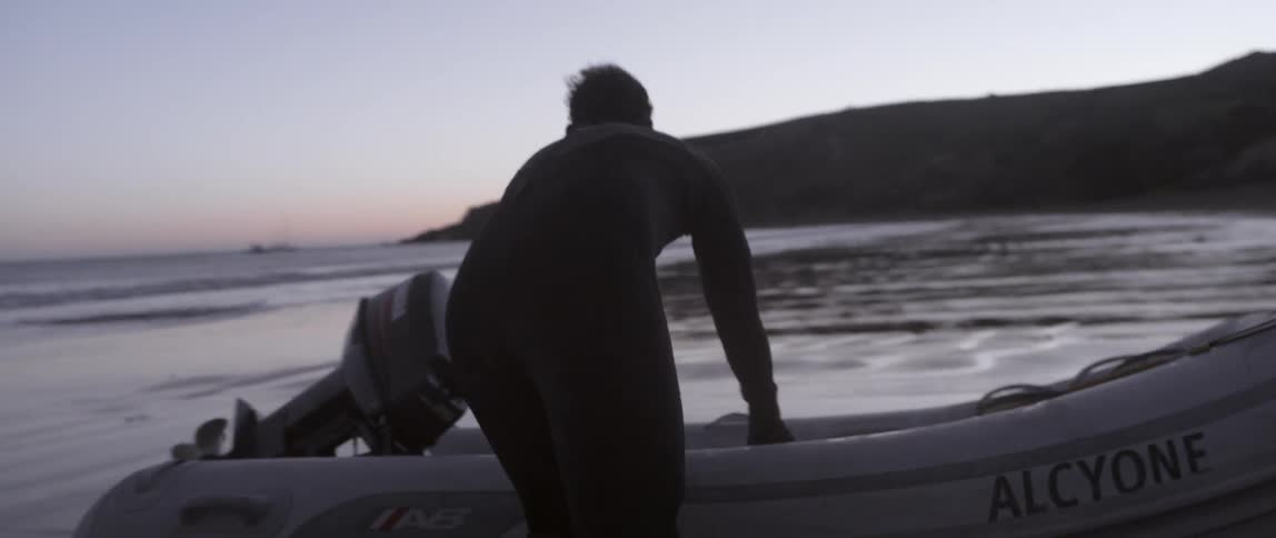 A man is loading items in a raft on the beach at dawn